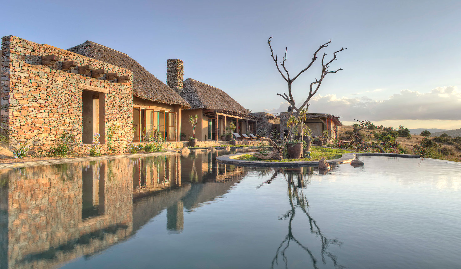 Lengishu House infinity pool overlooking Borana Conservancy at golden hour, Laikipia Kenya, with giraffe on the plain below